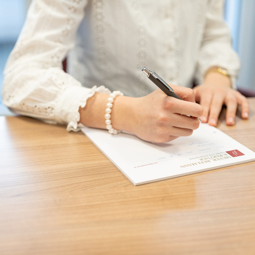 Nahaufnahme einer Frau, die an einem Holztisch mit einem Stift Unterlagen zur Steuerberatung oder Finanzplanung ausfüllt.