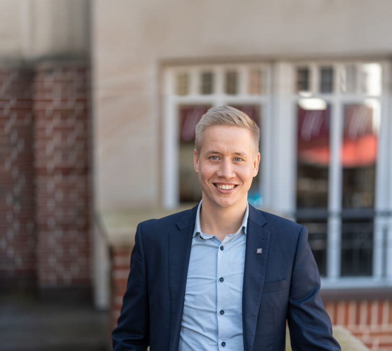 Jens Höveler, Partner von Meyer, Beelmann & Partner, lächelt in einem Porträt vor einem modernen Bürogebäude in die Kamera